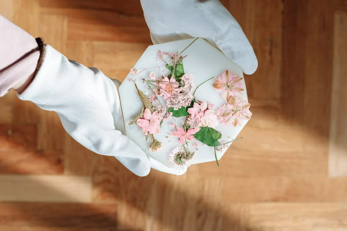Gloved hands holding a hexagonal resin piece with dried pink and white flowers